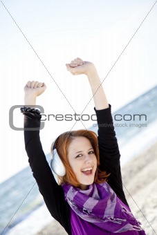 Portrait of red-haired girl with headphone on the beach.