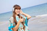 Young brunet girl with headphones on the beach.