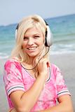 Young blonde girl with headphone on the beach.
