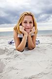 Beautiful blond girl lying on sand at the beach in rainy day.