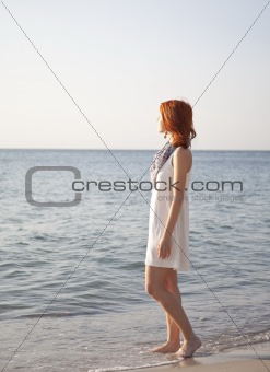 Beautiful red-haired girl at sunrise on the beach.