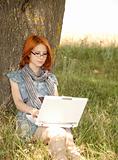 Young redheaded woman using laptop outdoors