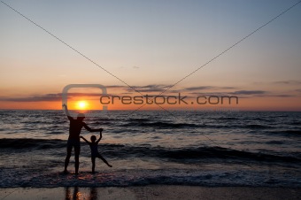 Silhouettes of father and his douther on beach at sunset