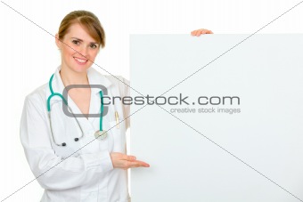 Smiling  medical doctor woman pointing on blank billboard
