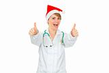Happy medical doctor woman in Santa hat showing thumbs up gesture
