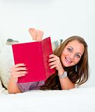 Smiling attractive woman lying on sofa and peeping out from book
