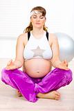 Concentrated beautiful pregnant woman doing yoga exercises on floor at home
