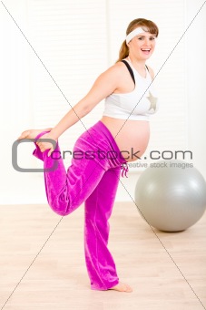 Smiling attractive pregnant woman making gymnastics at living room
