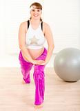 Smiling beautiful pregnant woman doing stretching exercises at home
