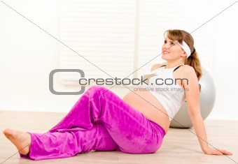 Smiling beautiful pregnant female making gymnastics at living room
