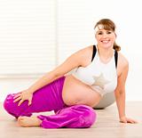 Smiling beautiful pregnant woman doing stretching exercises on floor 
