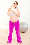 Smiling pregnant woman wiping her face with towel after exercising at home
