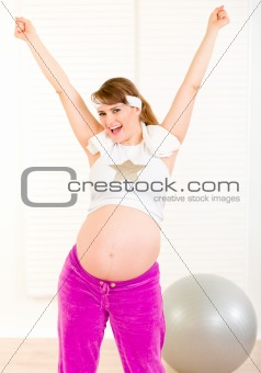 Pleased attractive pregnant woman in sportswear with hands raised  up
