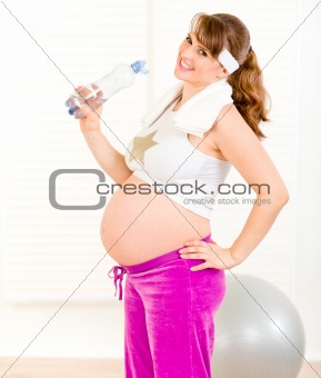 Smiling beautiful pregnant woman in sportswear holding bottle of pure water
