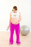Pregnant woman in sportswear holding bottle of water and looking on belly
