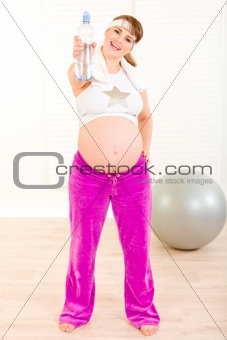 Happy beautiful pregnant female in sportswear holding bottle of pure water
