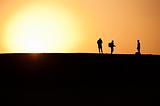 Three people silhouetted in sunset