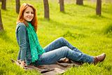 Beautiful red-haired girl sitting at green grass at park. 