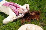 Brunette girl with headphone lies in the park.