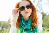 Beautiful red-haired girl in sunglasses at the park.