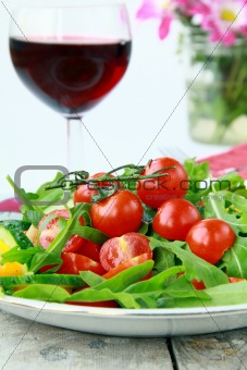 salad with arugula and cherry tomatoes with a glass of wine in the background