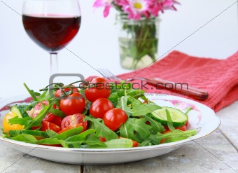 salad with arugula and cherry tomatoes with a glass of wine in the background