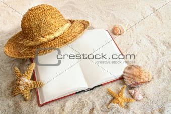 Book with straw hat and seashells in sand