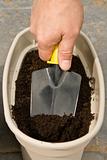 man's hand with a trowel digs in a planter to plant seeds