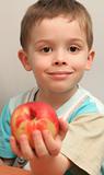 The boy holds a peach in a hand and smiles