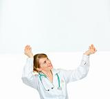 Smiling medical doctor woman looking at blank billboard
