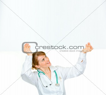 Smiling medical doctor woman looking at blank billboard
