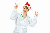 Happy medical doctor woman in Santa hat showing victory gesture 
