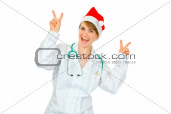 Happy medical doctor woman in Santa hat showing victory gesture 
