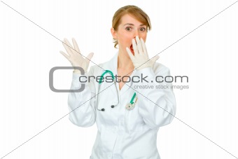 Shocked female doctor in medical gloves holding hand near mouth
