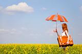 Redhead enchantress with umbrella and suitcase at spring rapeseed