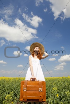 Redhead enchantress with suitcase at spring rapeseed field.