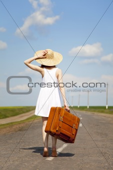 Lonely girl with suitcase at country road.