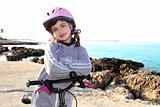 bicycle little happy girl pink helmet in rocky sea