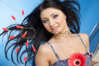 Young woman with flower lying back on blue hood in petals of New car