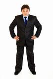 Full length portrait of strict businessman with hands on hips attentively looking at you

