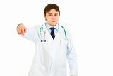 Smiling young medical doctor pointing finger down
