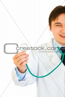 Smiling young medical doctor holding up stethoscope. Close-up.
