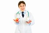 Smiling medical doctor with pills in one hand and apple in other
