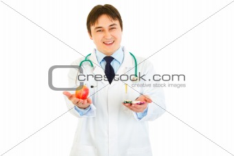 Smiling medical doctor with pills in one hand and apple in other
