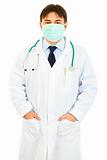 Medical doctor with mask on face holding hands in pockets
