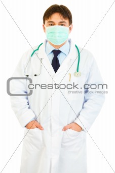 Medical doctor with mask on face holding hands in pockets

