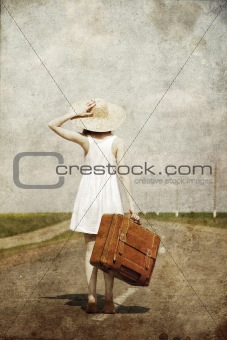 Lonely girl with suitcase at country road.
