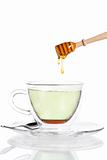 honey drops from a honey dipper in glass cup with green tea