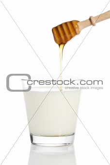 honey falling from a honey dipper in a jar with milk