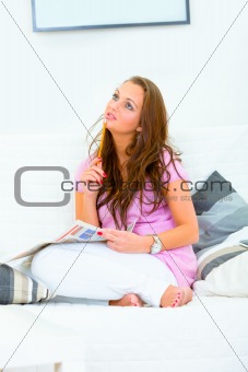 Concentrated woman sitting on sofa and doing crosswords
